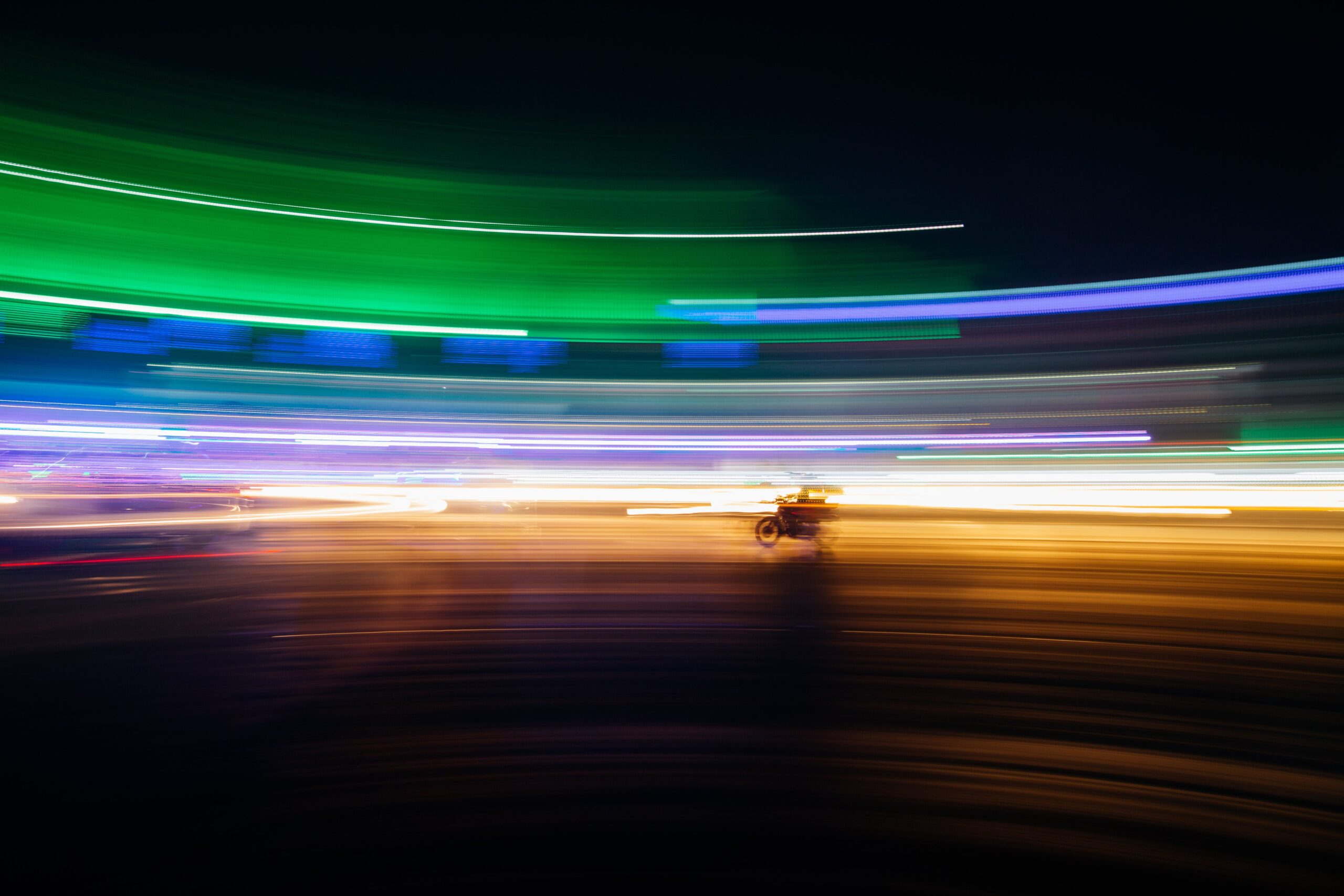 Time lapse picture of a motorbike against bright neon light trails.